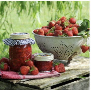 A bowl of strawberry jam surrounded by jars, elegantly displayed on a wooden table.
