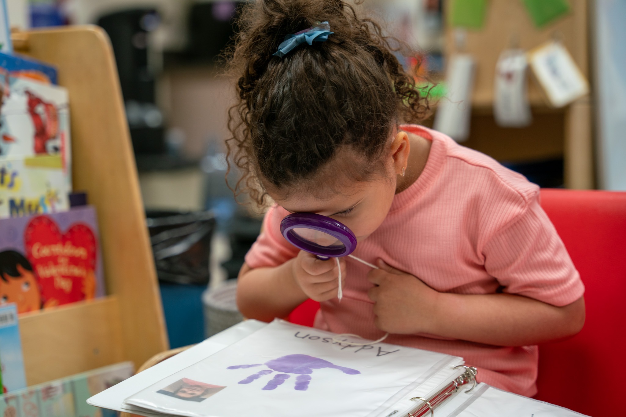 Picture of a preschool kid looking at a binder with a magnifying glass