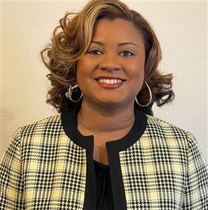 A woman with curly hair wearing a black and white checkered blazer and large hoop earrings smiles at the camera against a plain background.