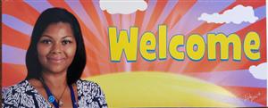 A woman stands next to a colorful background featuring the word 'Welcome' in large yellow letters, with a sun and clouds illustrated behind her.