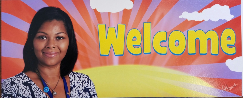 A woman stands next to a colorful mural that features the word 'Welcome' in large yellow letters against a backdrop of a rising sun and clouds.