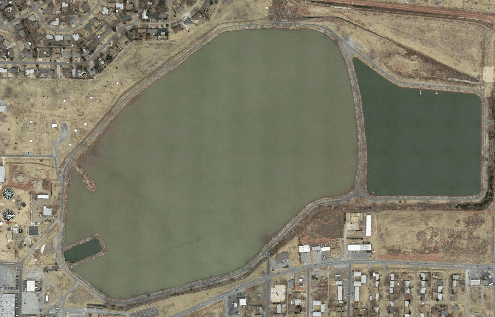 An aerial view of two large bodies of water surrounded by dry land and a nearby urban area.