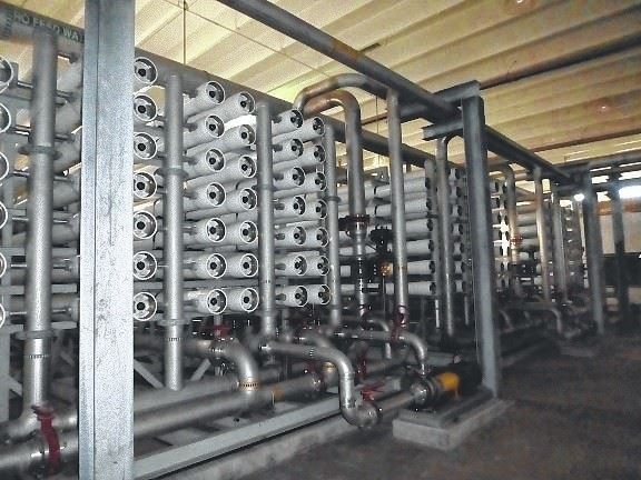 A large industrial setup featuring multiple rows of cylindrical filtration units and interconnected piping, housed under a wooden ceiling.