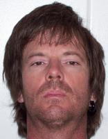 A headshot of a man with medium-length brown hair and a serious expression, facing directly towards the camera.