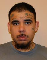 A man with tattoos on his face and neck, wearing a gray shirt, looking directly at the camera.