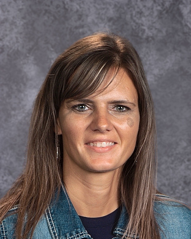 A woman wearing a denim jacket over a blue shirt, standing confidently with a neutral background.
