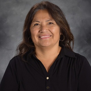 Woman with brown hair smiling, standing against a gray background, wearing a black shirt with buttons.