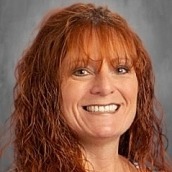 A woman with long red hair smiles at the camera against a gray background.