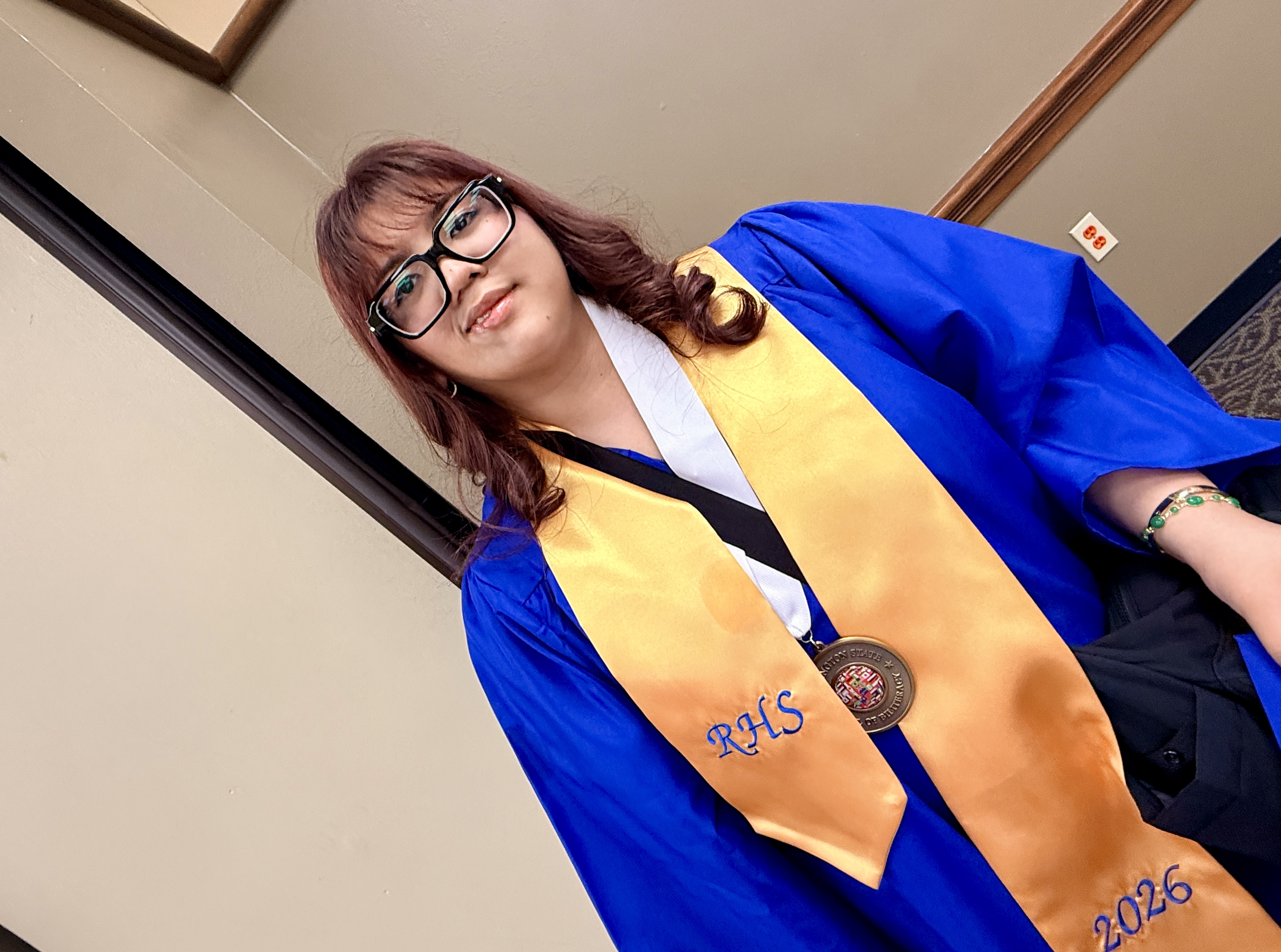 Woman in a blue graduation gown and gold stole with a medal and the words "RMS 2026" on it.