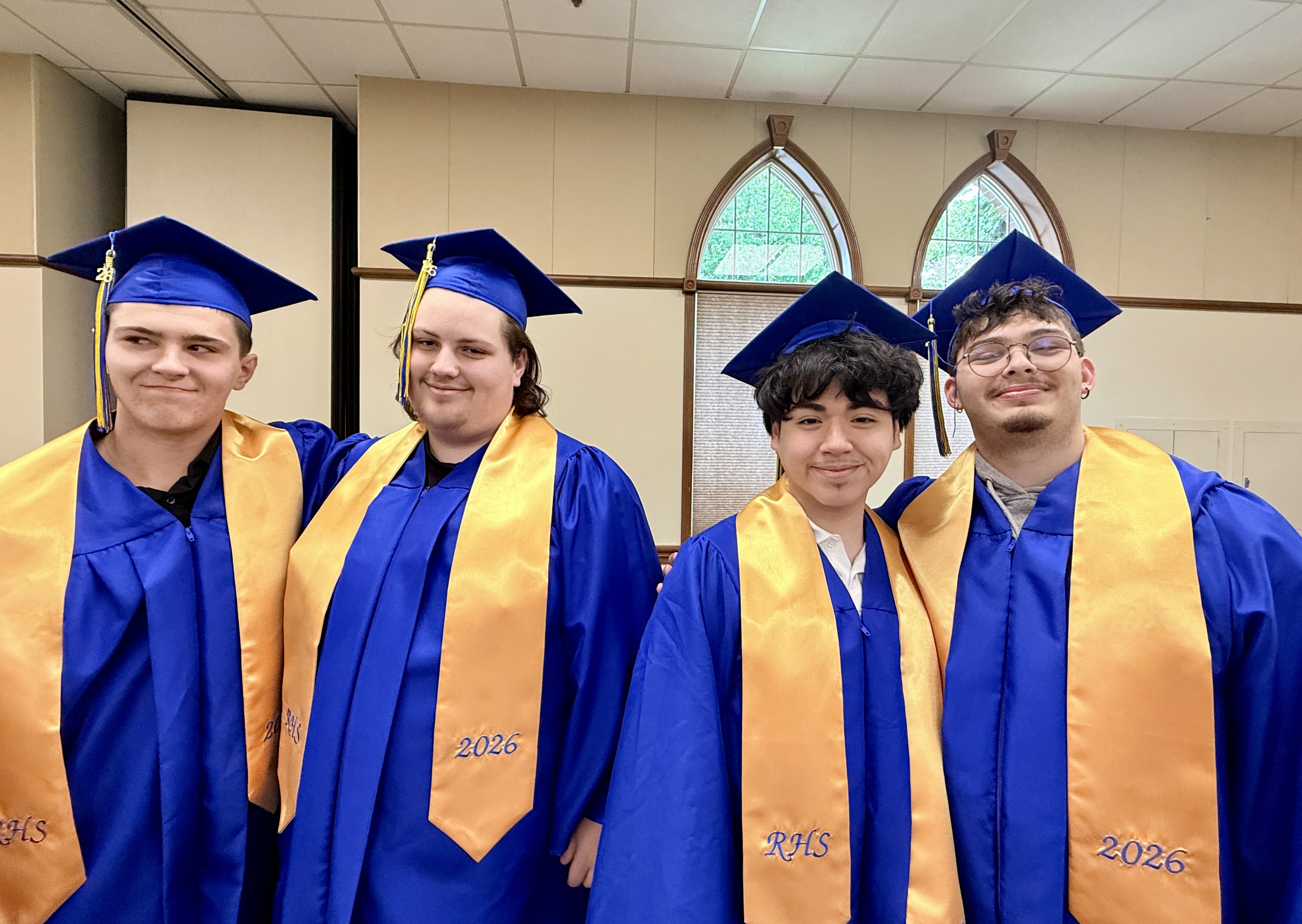 Four people in caps and gowns, standing together with smiles, possibly at a graduation.
