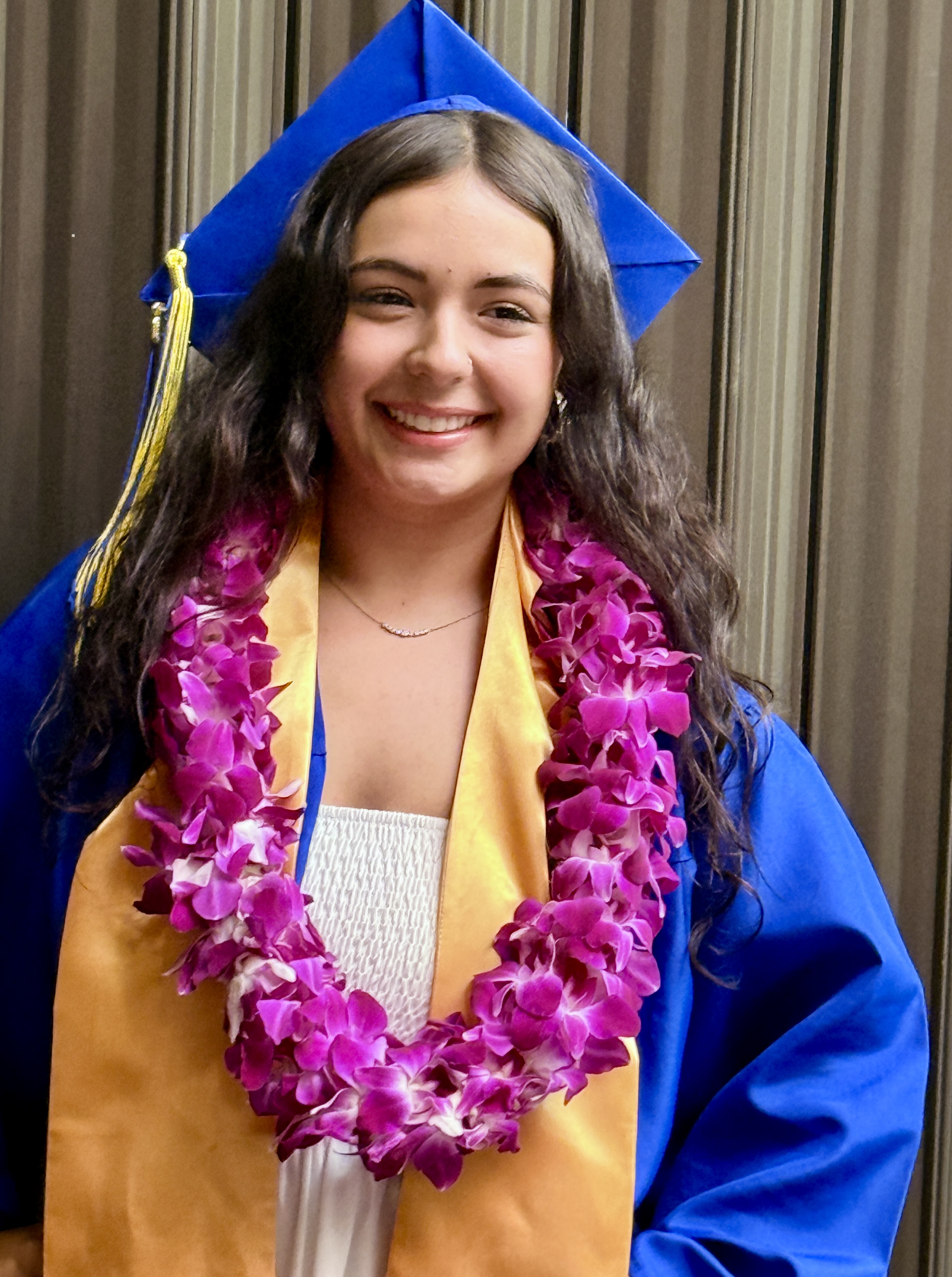 A woman in a blue and gold graduation gown with a blue cap poses for a photo.