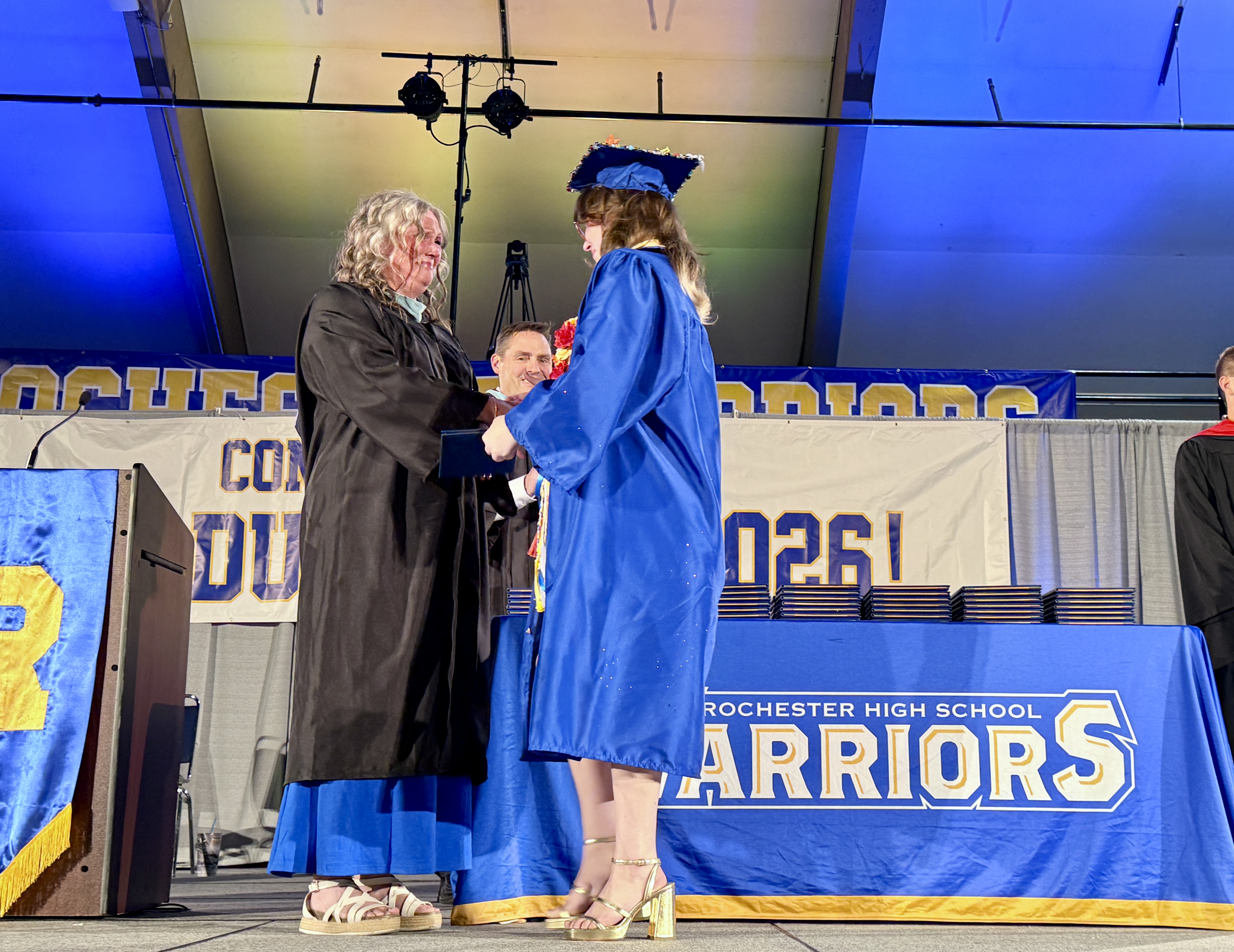 Two people on stage, one in a cap and gown, shaking hands with a person in a black gown.
