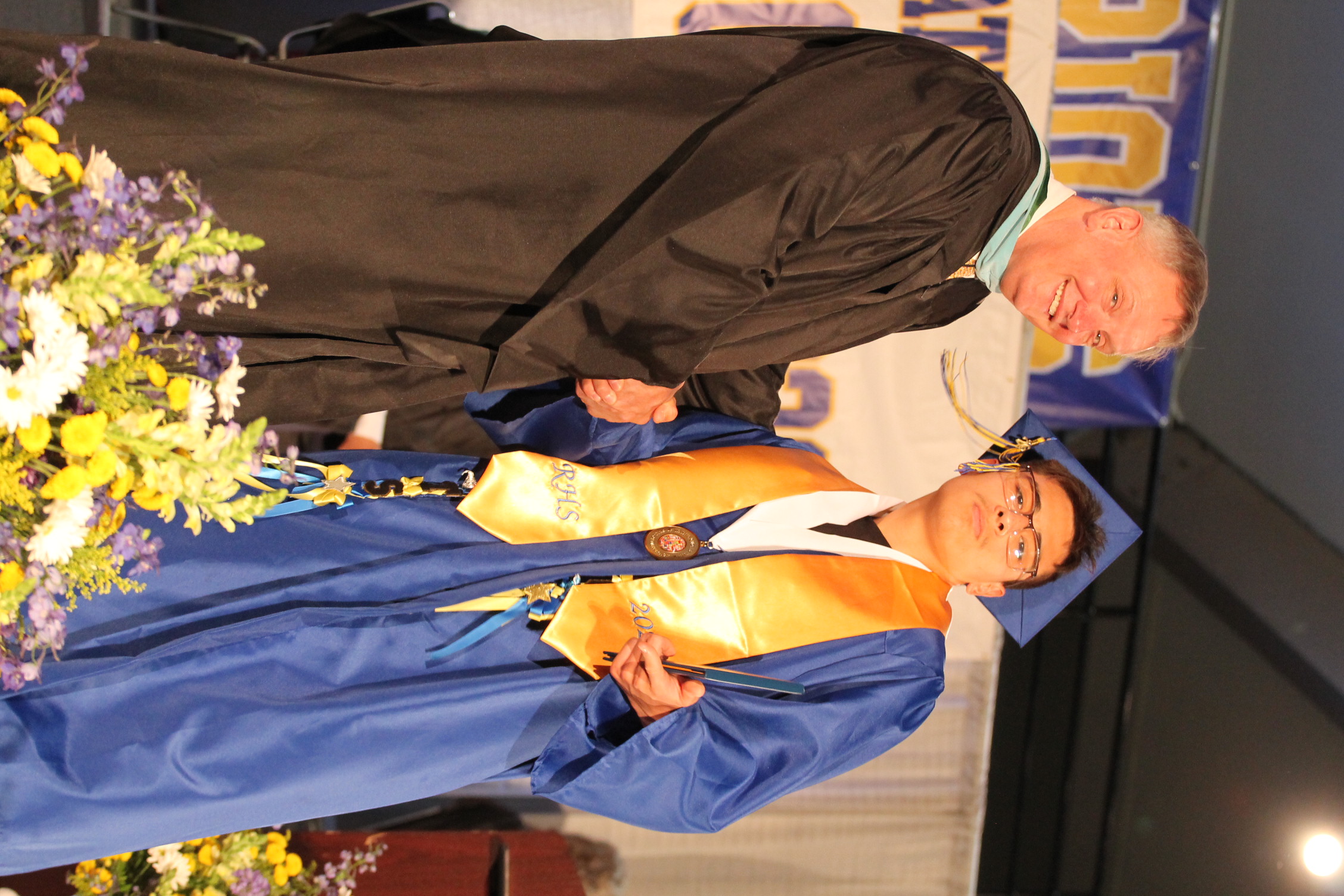 Two people on a stage in academic robes. The man is receiving a medal from the other man.