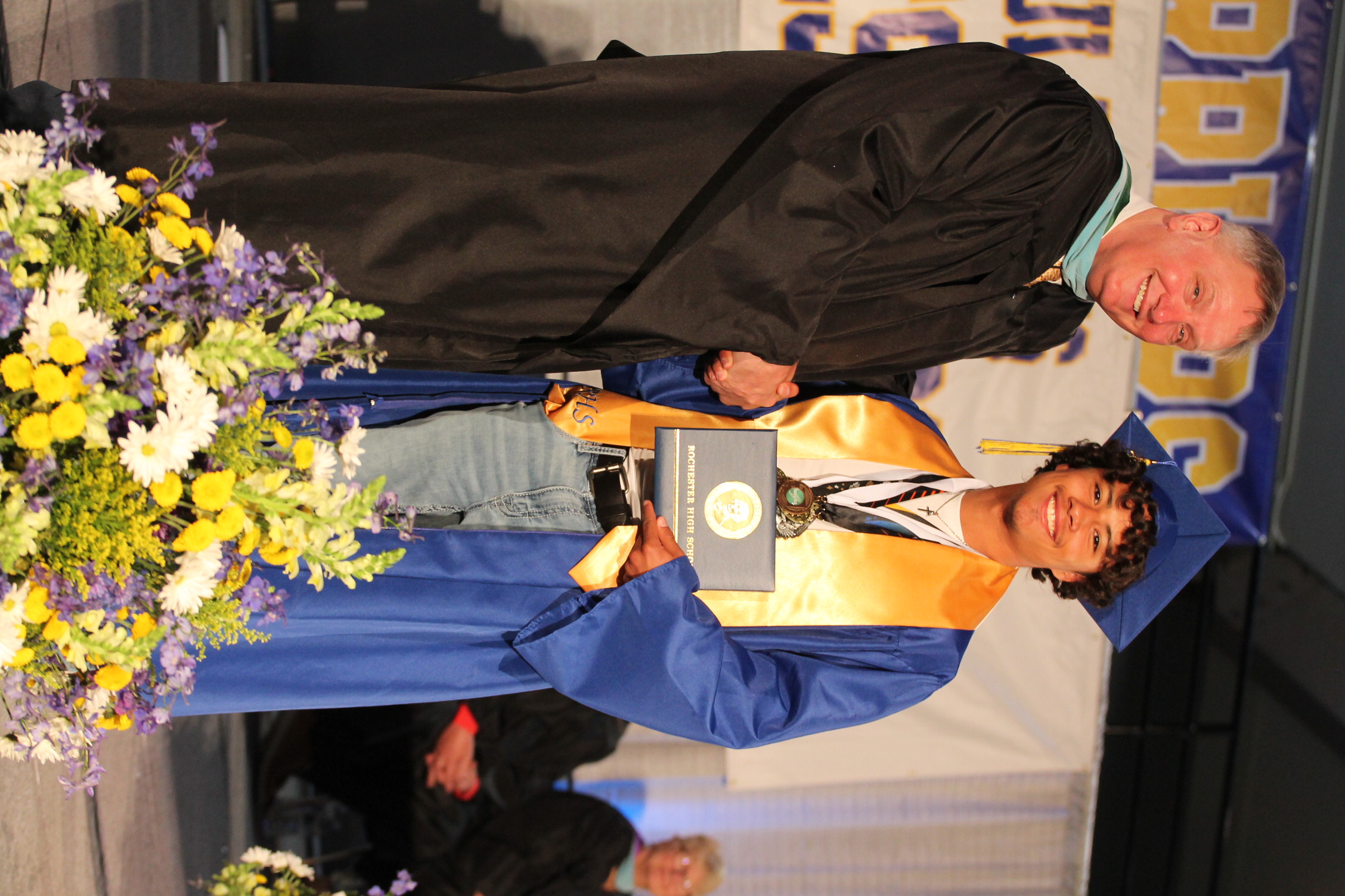 A person in a cap and gown holds an award and shakes hands with a man in a cap and gown.