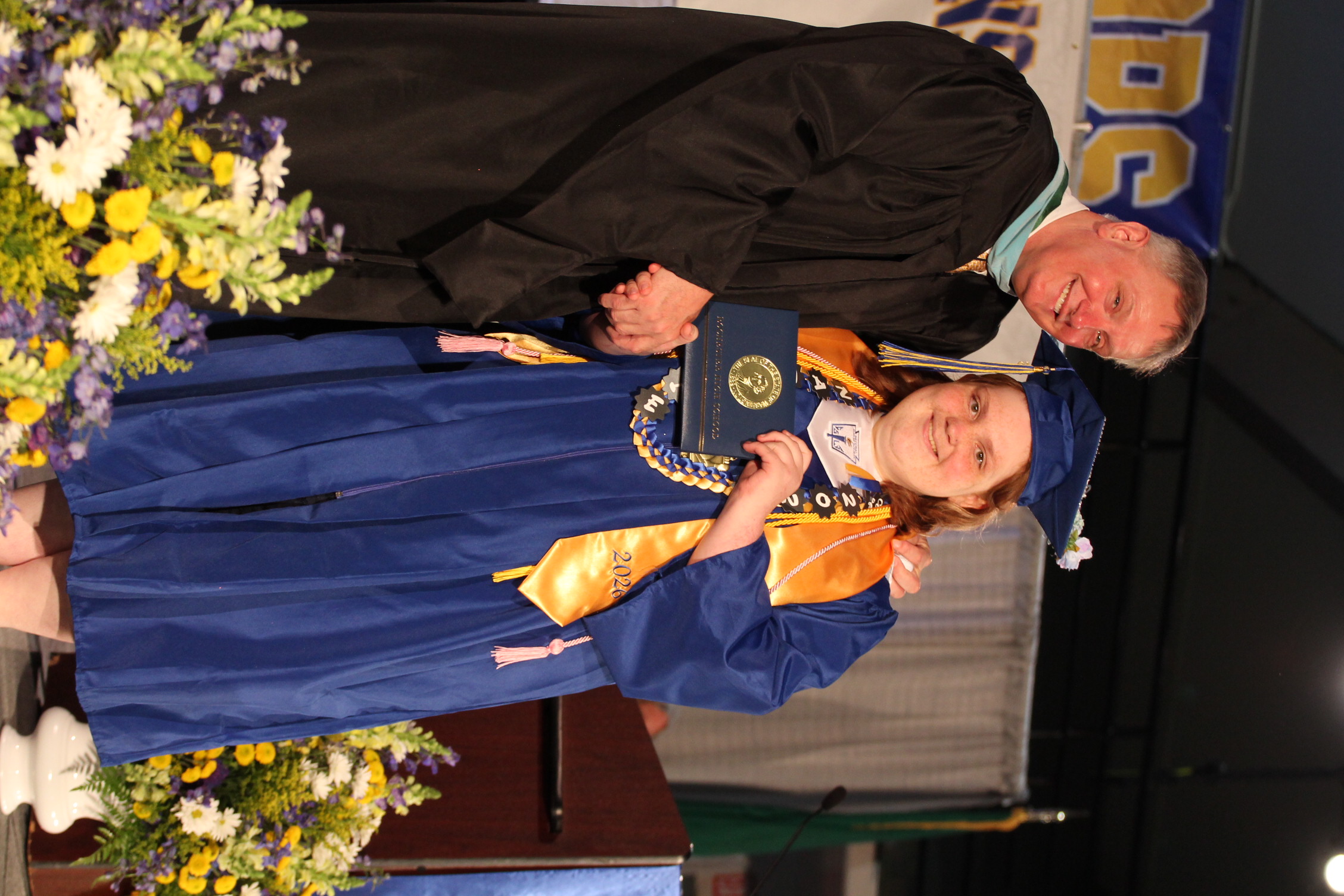 A man in a black robe hands a diploma to a woman in a blue gown on a stage.