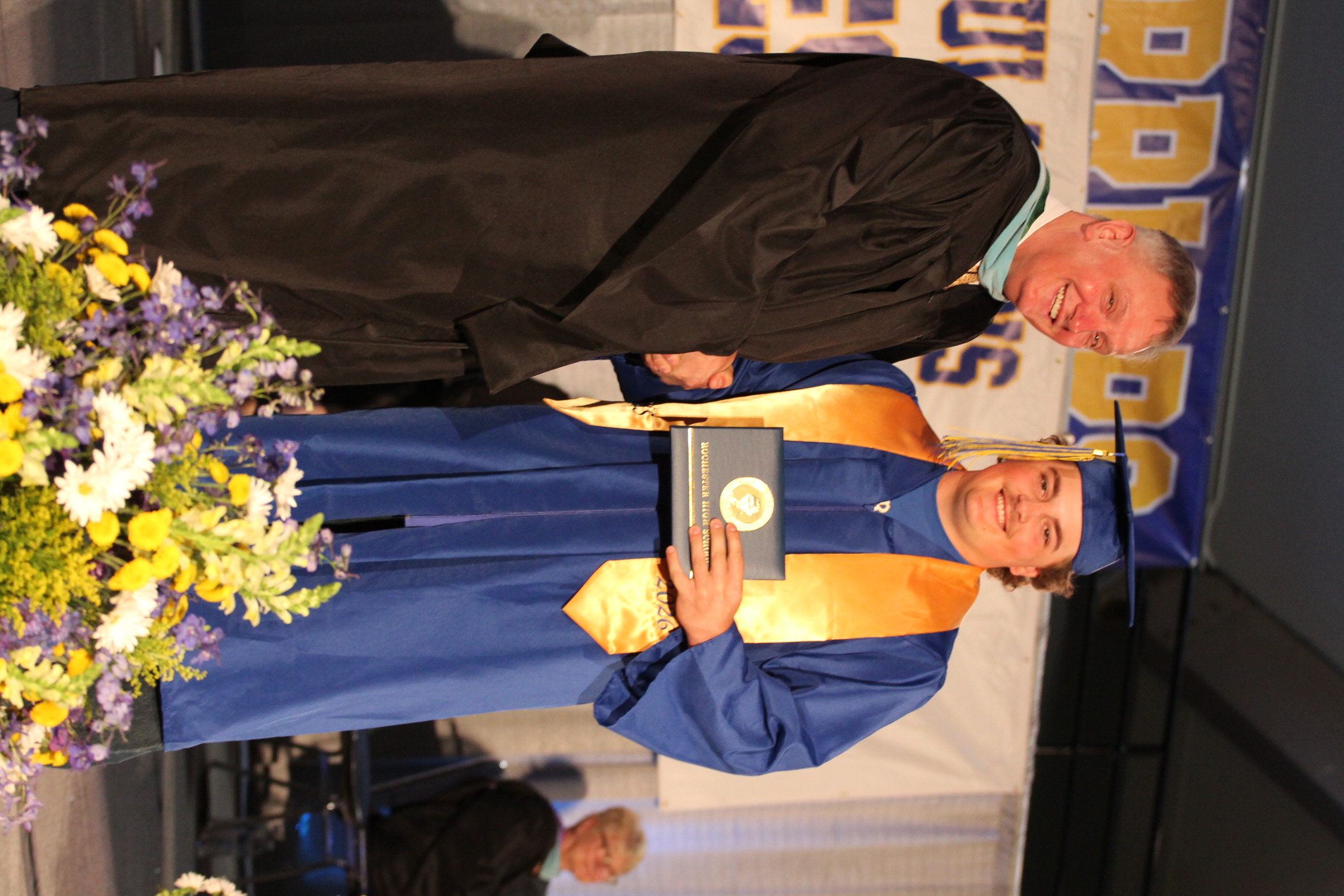 A man in a cap and gown receiving an award from another man on a stage.