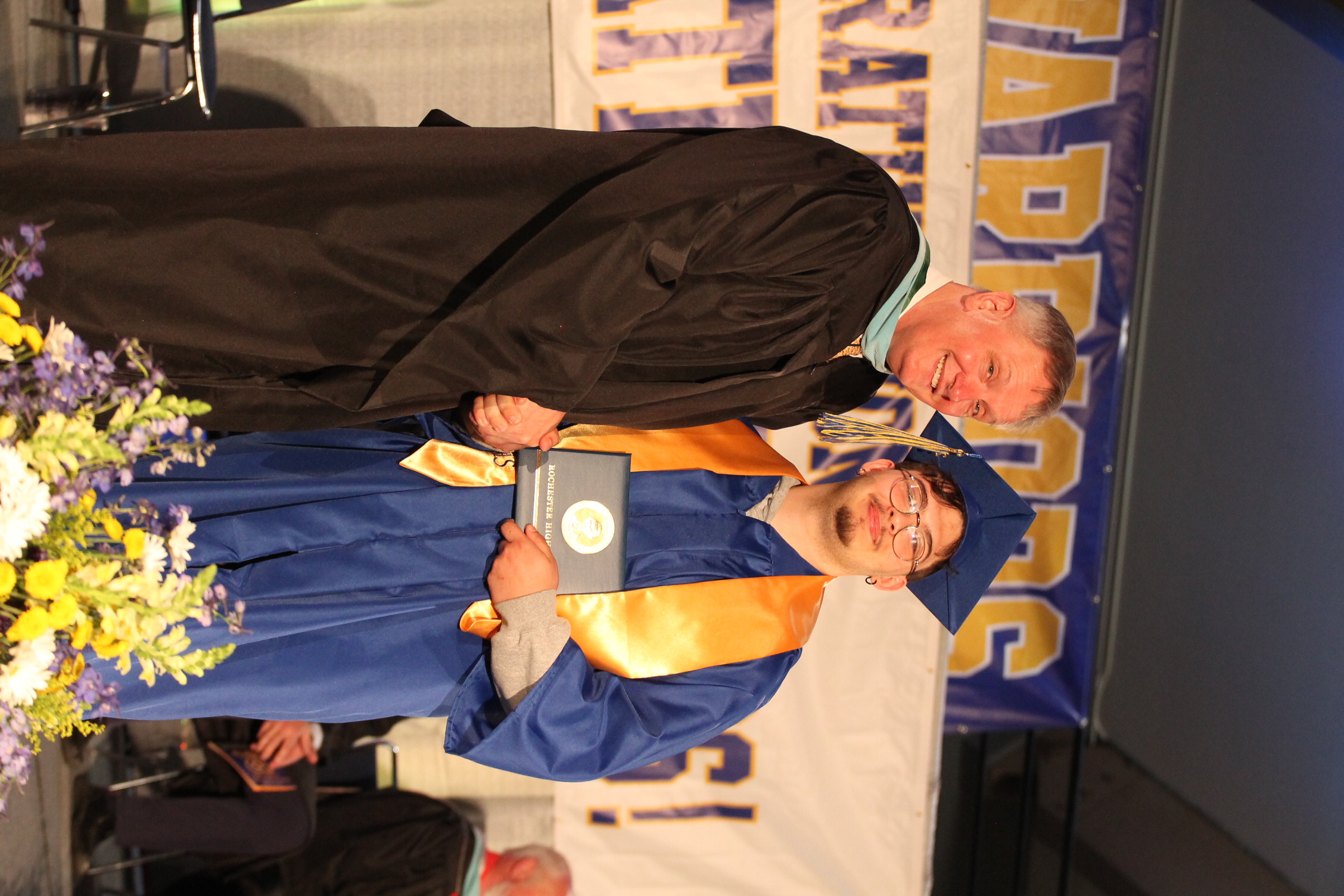 A man in a cap and gown stands next to a faculty member holding a framed certificate.