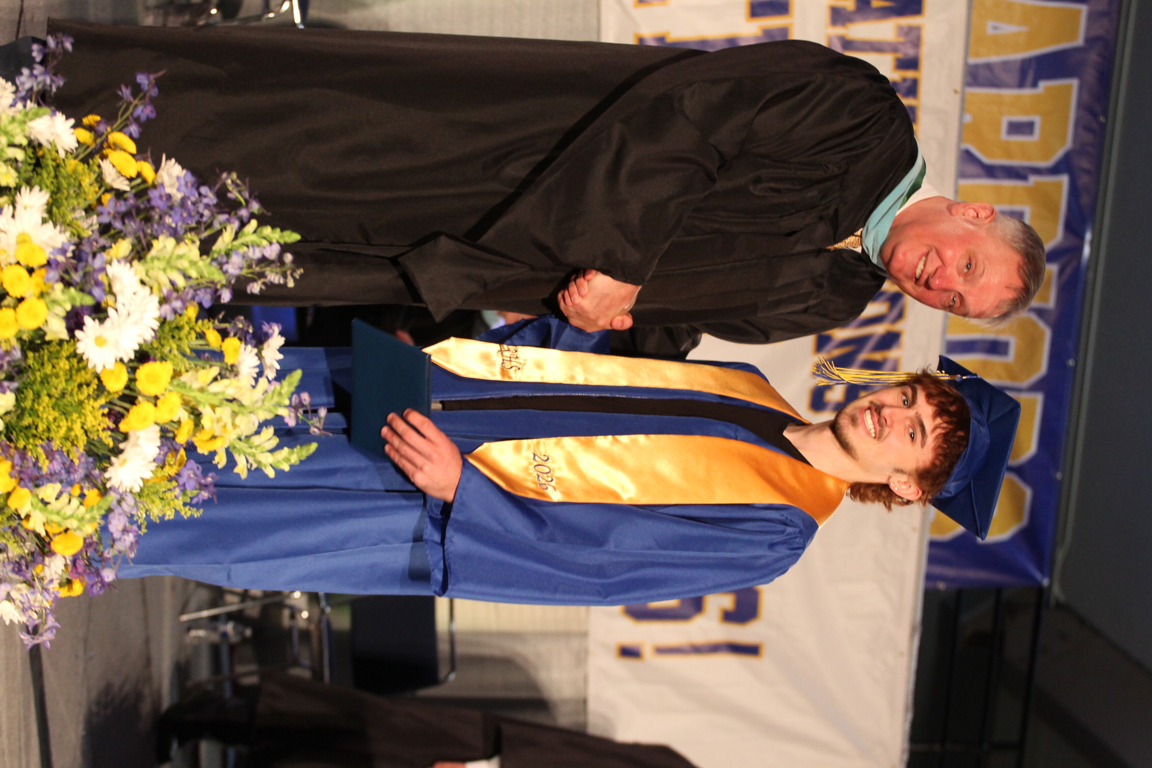 Man in cap and gown receiving diploma from a faculty member during a graduation ceremony.