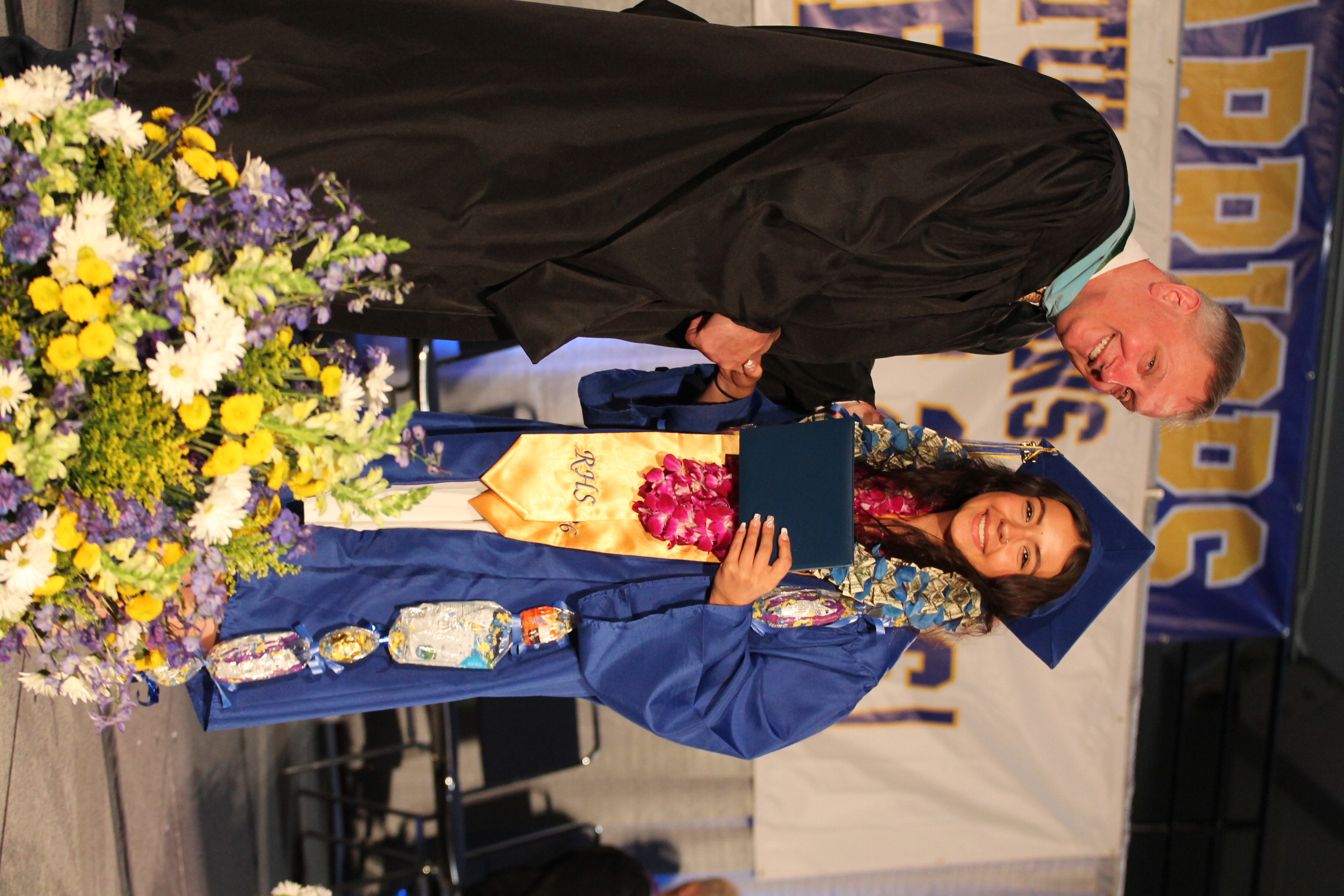 A man and a woman on a stage, with the man presenting a diploma to the woman. Both wear academic regalia.