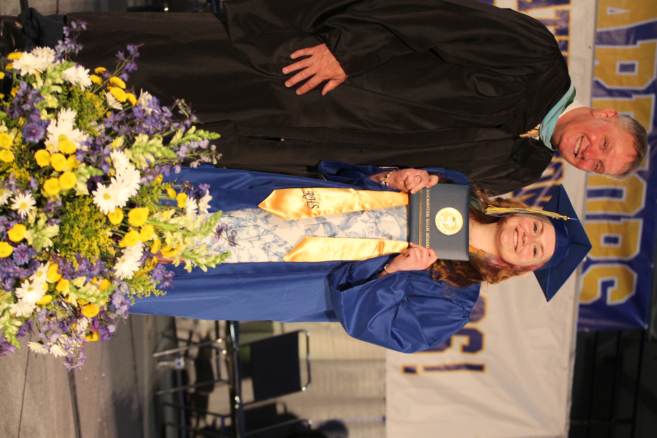 A man in a black gown stands next to a woman in a blue gown holding a certificate.