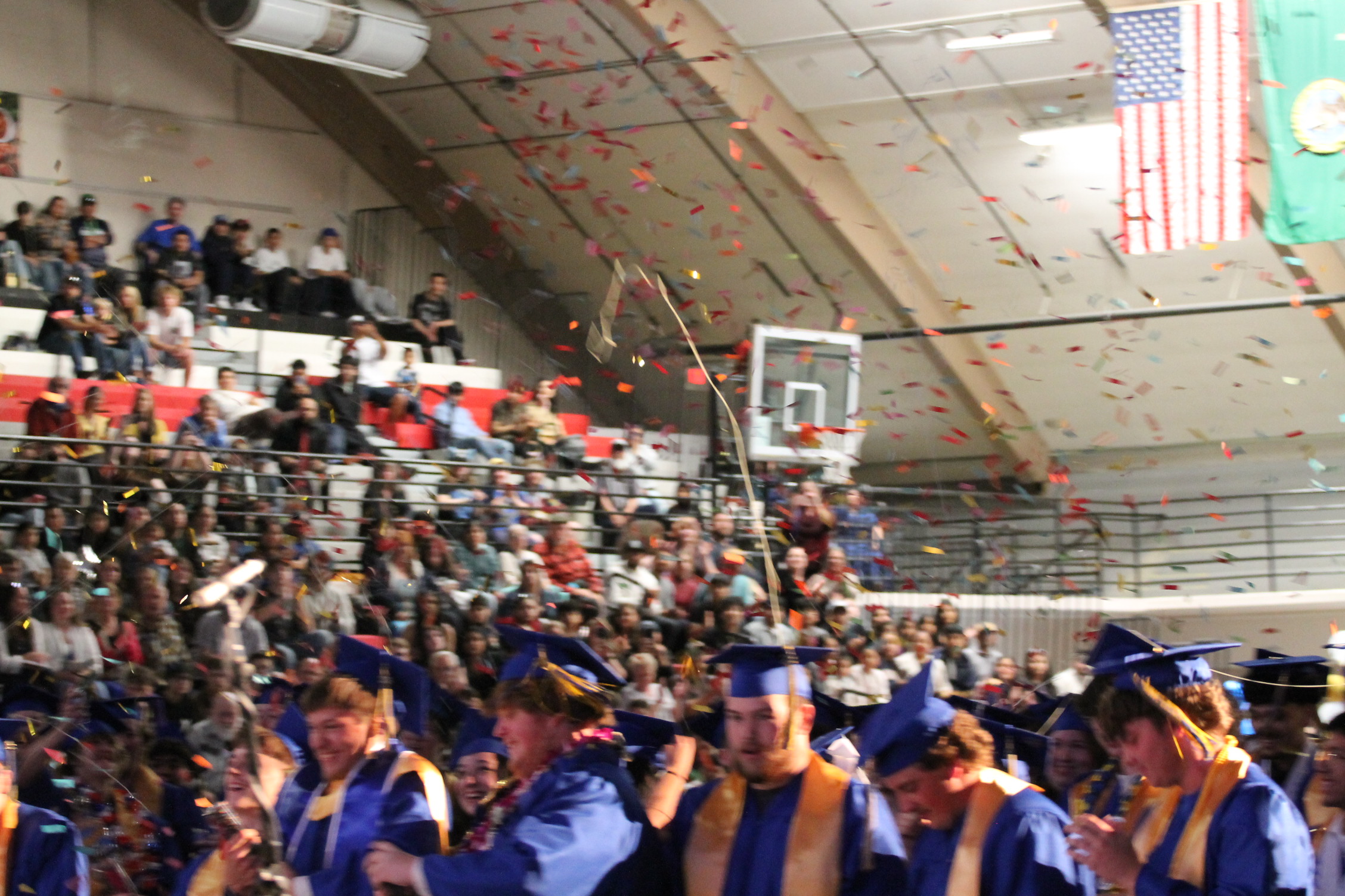 Confetti falling over a crowd of people wearing blue caps and gowns, attending an indoor ceremony.