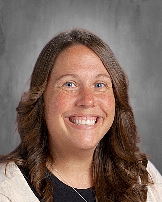 Woman with brown hair smiling at the camera. She wears a white sweater over a black shirt and a silver necklace.