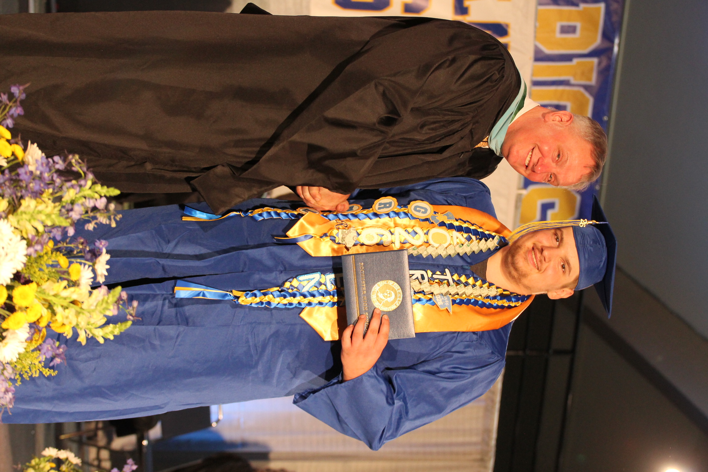 A man in a graduation gown and cap receiving a diploma from another man during a graduation ceremony.