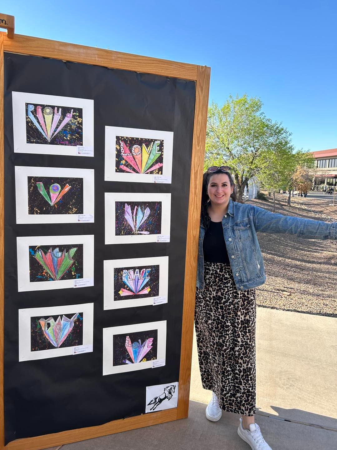 Art teacher posing next to an art board filled with student artwork