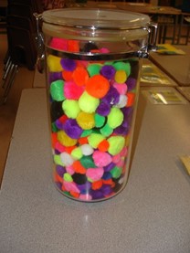 A jar filled with vibrant pom poms sits on a table, showcasing a variety of colors and textures in a playful arrangement.