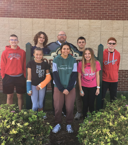 A group of students smiling and posing together in front of a large sign, capturing a moment of camaraderie.