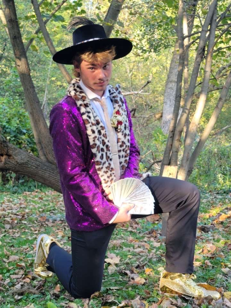 A man in a purple suit and gold shoes sits on the ground, exuding a stylish and confident demeanor.