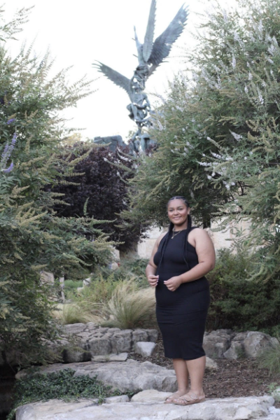 A woman in a black dress poses elegantly in front of a statue, showcasing a blend of art and fashion.