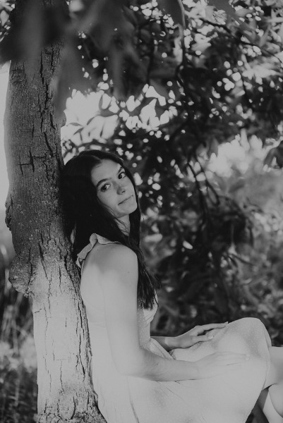 A woman sits gracefully on a tree branch, surrounded by lush greenery in a serene woodland setting.