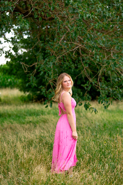 A young woman in a pink dress stands gracefully in a vibrant green field, embodying beauty and serenity.