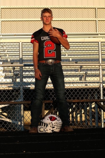 A young man in a football uniform stands confidently on a bleacher, showcasing team spirit and athleticism.