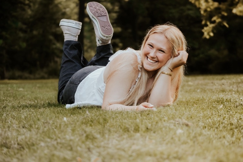 A beautiful blonde woman reclines on the grass in a serene park, enjoying a moment of relaxation in nature.