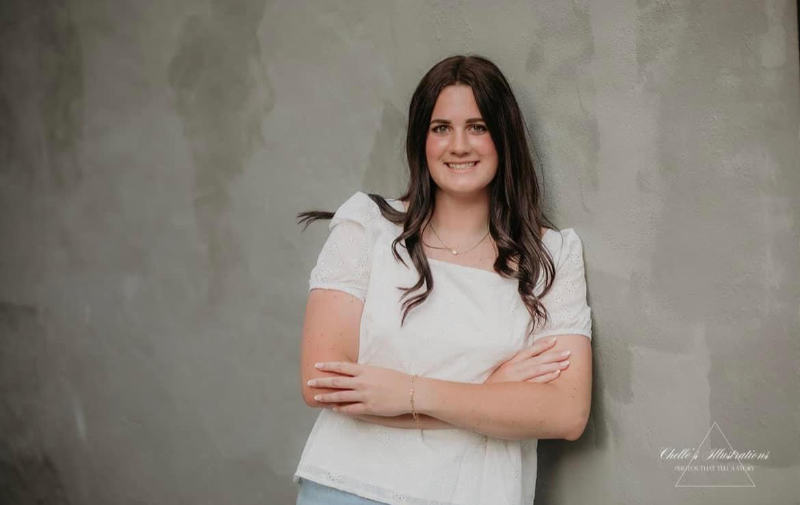 A beautiful young woman casually leans against a wall, exuding confidence and grace in her posture.