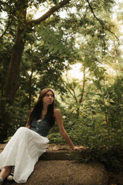 A woman seated gracefully on a stone wall, surrounded by a serene outdoor setting.