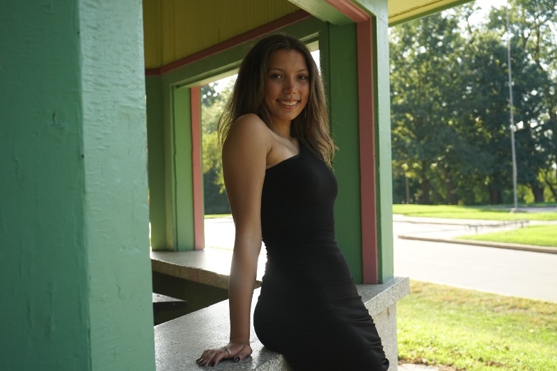 A woman in a black dress elegantly poses for a photo, showcasing her style and confidence.