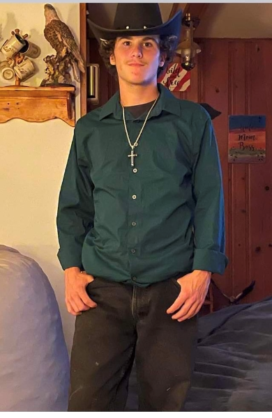 A young man in a cowboy hat and green shirt stands confidently, embodying a rustic and adventurous spirit.
