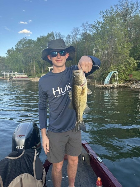 A man wearing a hat and sunglasses proudly holds a large bass fish, showcasing his catch of the day.