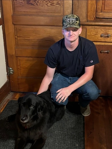 A man kneels beside a black dog, creating a moment of connection and companionship between them.