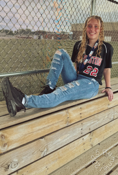 A girl sits on a bench, gazing thoughtfully in front of a wooden fence, surrounded by a serene outdoor setting.