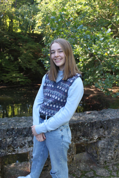 A girl dressed in jeans and a cozy sweater, standing confidently with a smile.