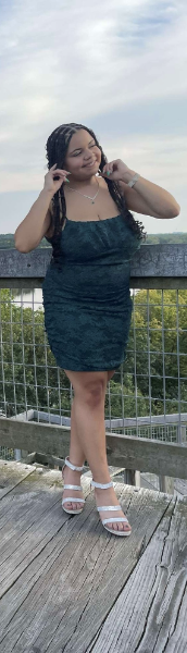A woman in a blue dress stands gracefully on a wooden deck, surrounded by a serene outdoor setting.