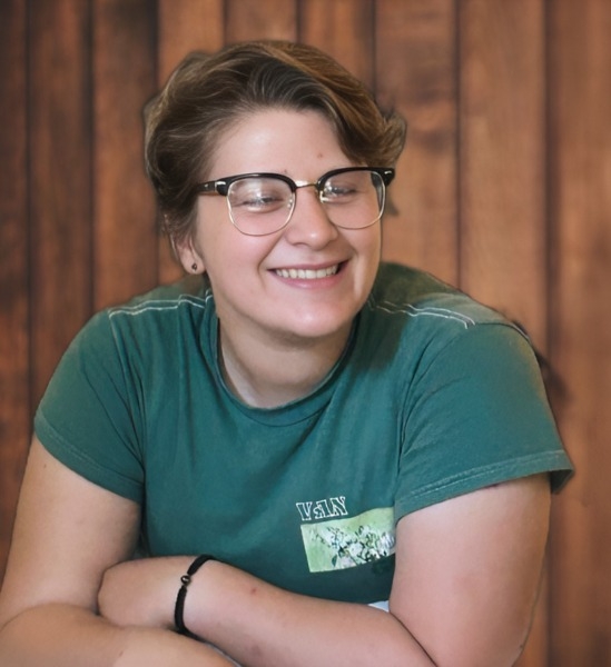 A smiling woman in glasses and a green shirt, exuding warmth and positivity.