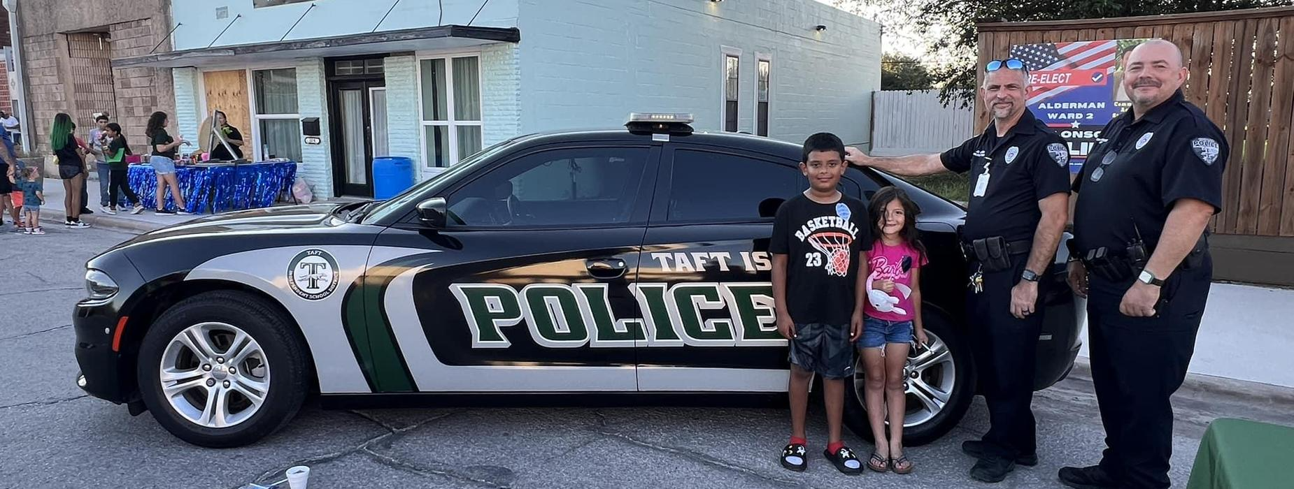 Two police officers and a child smile together in front of a police car, showcasing community engagement and safety.