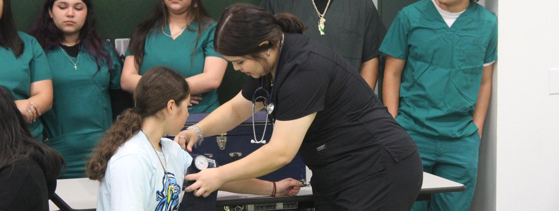 A woman in green scrubs assists a man seated in a chair, providing care and support in a medical setting.