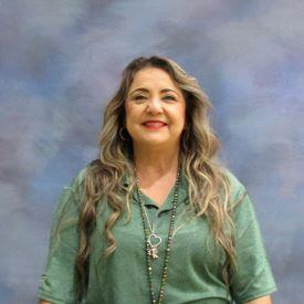 A woman wearing a green shirt and jeans stands confidently, showcasing a casual yet stylish outfit.