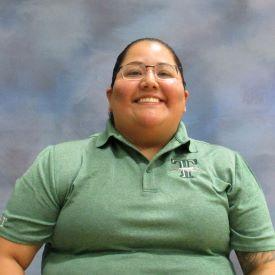 A woman wearing a green shirt is seated on a chair, appearing relaxed and contemplative.